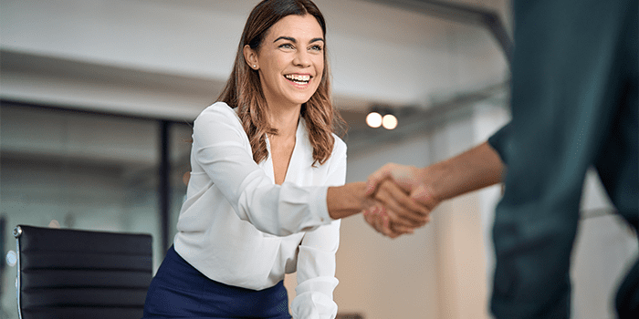 Happy mid aged business woman manager handshaking greeting client in office. Smiling female executive making successful deal with partner shaking hand at work standing at meeting table.